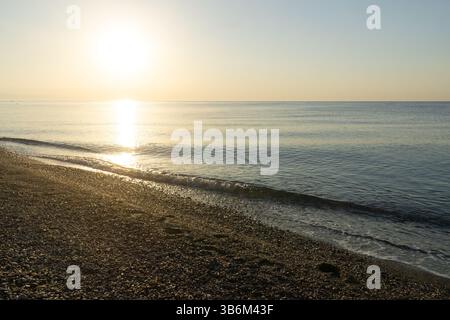 Onde dolci che lavano una spiaggia di ciottoli durante un'alba dorata su un mare calmo Foto Stock