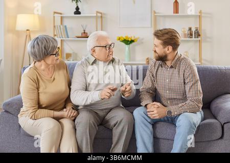 Famiglia di genitori anziani e figlio adulto seduti sul divano a casa e che parlano insieme. Foto Stock