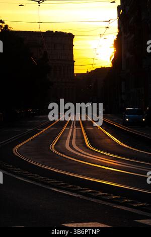 La luce del tramonto si riflette sulle rotaie del tram in via Labicana, con il Colosseo sagomato sullo sfondo di Roma, Italia. Foto Stock