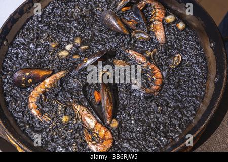 Primo piano di paella nera con gamberetti, cozze e altri frutti di mare, cucinati e pronti per essere serviti in una paella tradizionale Foto Stock