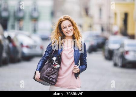 Cane Chihuahua trasportato in sacchetto dell'animale domestico. Cane carino in trasparente trasportino da viaggio per animali domestici. Donna caucasica che tiene una borsa da trasporto con animale domestico sulla strada. Il proprietario Foto Stock