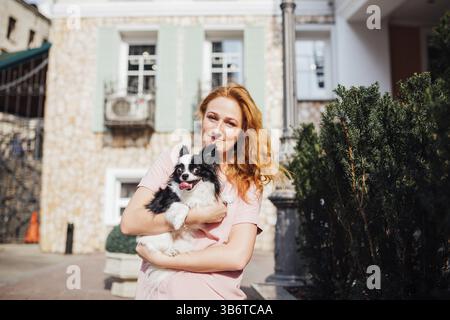 Il tema è l amicizia di uomo e animali. Giovane e bella con i capelli rossi donna caucasica tenendo un cane di razza Chihuahua in prossimità di una costruzione casa in Foto Stock