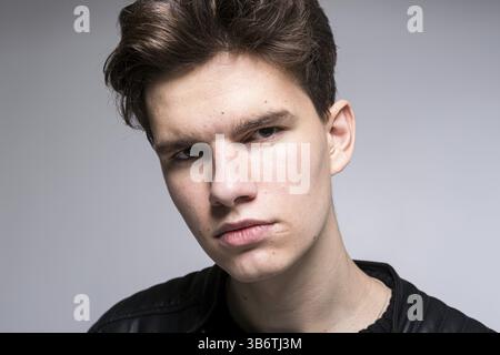 Grandangolo. Ripresa in studio. Giovane ragazzo caucasico modello in abiti neri che posa in studio. Giacca in pelle per adolescenti in piedi davanti allo schienale bianco Foto Stock