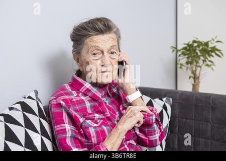 Tema la persona anziana usa la tecnologia. Maturo felice sorriso capelli grigi attivi rughe caucasiche donna seduto a casa nel soggiorno sul divano e utilizzando un Foto Stock