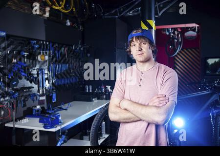 Servizio di trasporto per piccole imprese e biciclette. ritratto di un giovane uomo in un berretto che posa sullo sfondo di un laboratorio di biciclette e di uno strumento per sistemarsi Foto Stock