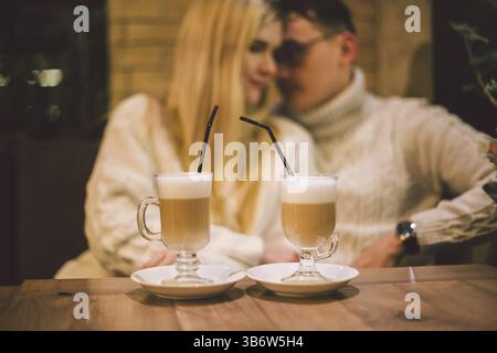 Giovane coppia felice innamorata nel caffè, uomo e donna insieme sorridono abbracciando, bevendo caffè. Coppia che parla al Cafe in inverno. Coppia felice che si diverte con un c Foto Stock