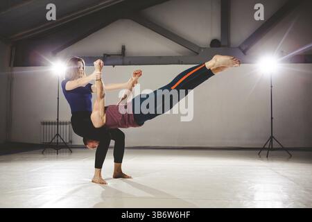 Il tema di Acroyoga e Yoga pone. Acroyogis praticante. con lo studio di retroilluminazione. La donna Base mantiene l'uomo volantino in posizione orizzontale S Foto Stock