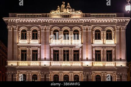 Un edificio storico splendidamente illuminato di notte, che mostra intricati dettagli architettonici e sculture sul tetto. La facciata è ornata Foto Stock