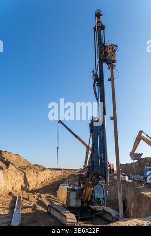 La palificatrice vibrante gialla rimuove l'accatastamento di lastre Larssen dal terreno dopo il completamento dei lavori di scavo a grande profondità. Foto Stock