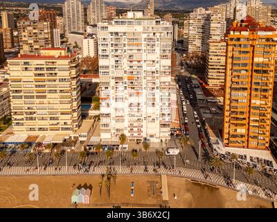 Fotografia aerea di Levante Beach, Benidorm, Spagna. L'immagine mostra una lunga spiaggia di sabbia ricurva con sabbia dorata e acque turchesi del Mar Mediterraneo. Alti hotel e condomini fiancheggiano la passeggiata. Vista invernale, fuori stagione. Il cielo è parzialmente nuvoloso. La fotografia è stata scattata da una posizione sopraelevata che si affacciava sulla costa e sull'area urbana. Foto Stock