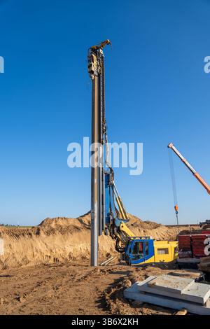 La palificatrice vibrante gialla rimuove l'accatastamento di lastre Larssen dal terreno dopo il completamento dei lavori di scavo a grande profondità. Foto Stock