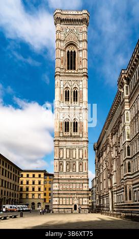 Un alto campanile ornato con disegni intricati, adagiato su un cielo blu con nuvole sparse. La torre presenta motivi di marmo colorati ed e' par Foto Stock