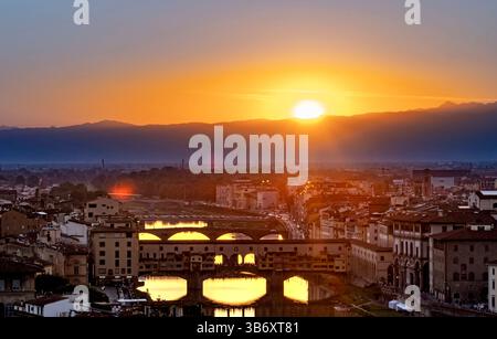 A stunning sunset over Florence, Italy, showcasing the Arno River and historic architecture. The sun dips behind the mountains, casting a warm glow on Foto Stock
