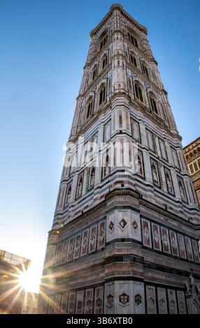 Un'alta torre decorata con intricati dettagli architettonici, adagiata su un cielo azzurro. Il sole splende brillantemente sullo sfondo, creando uno stendardo Foto Stock