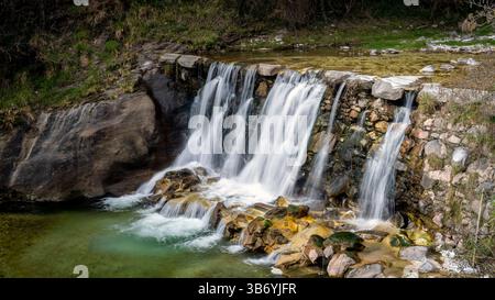 Una cascata serena che si getta sulle rocce in una piscina limpida, circondata da vegetazione lussureggiante. L'acqua scorre dolcemente, creando un'atmosfera tranquilla. Foto Stock