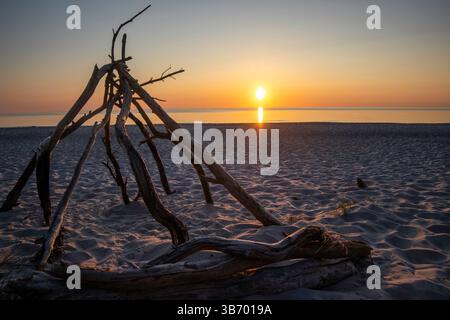 Uno splendido tramonto proietta calde sfumature sul Mar Baltico lungo la penisola dello Darß. Una struttura in legno di mare poggia sulla spiaggia sabbiosa, creando una tranquilla atmosfera Foto Stock