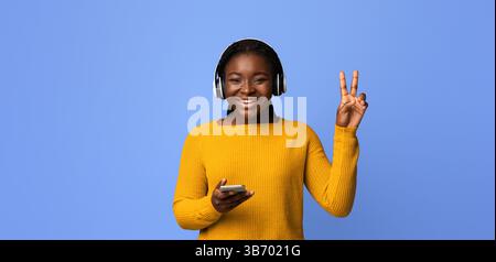 Ritratto di allegra giovane signora nera in cuffie wireless con Smartphone Foto Stock