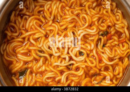 Primo piano di spaghetti di ramen istantanei appena cotti immersi in un ricco brodo rosso arancio, speziato con peperoncino. Foto Stock