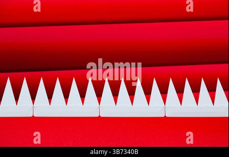 Denti bianchi appuntiti triangolari sporgenti in una fila di rosso, su uno sfondo a strisce rosse. Foto Stock