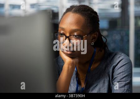 Tecnici del data center annoiati al lavoro che ispezionano gli attrezzi, svolgendo attività di manutenzione monotona. Donna stanca in un dipendente di server farm che esegue controlli di sistema per garantire la stabilità operativa Foto Stock