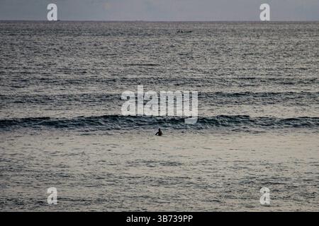 Ampia vista di una persona in mezzo all'oceano. Le tranquille onde dell'oceano si infrangono a Seminyak Beach, Bali, perfetta per rilassanti vedute costiere e spiaggia Foto Stock