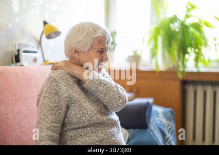 Donna anziana che soffre di mal di schiena seduta sul letto Foto Stock
