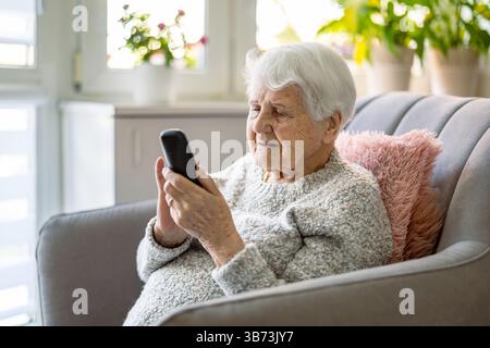 Senior donna utilizzando il telefono cellulare a casa Foto Stock