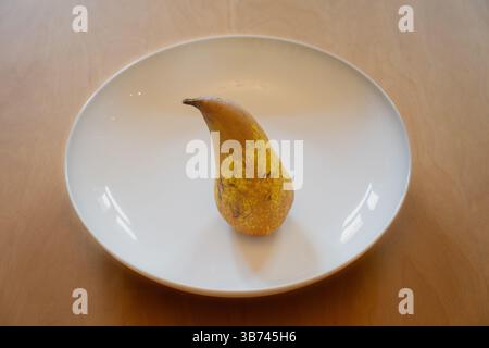 Una pera in piedi in un piatto bianco su un tavolo di legno Foto Stock