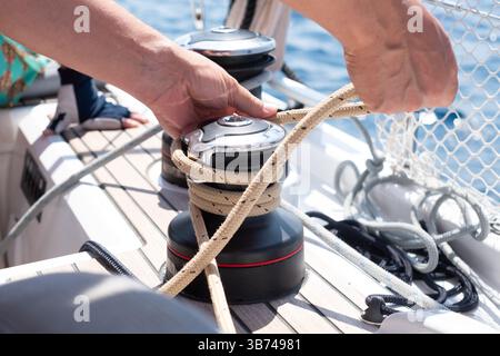 Uomo che lavora su corde e verricello per yacht a vela. Dettagli sull'equipaggiamento della barca a vela. Trasporto d'acqua, viaggi marittimi a tema vacanza. Foto Stock
