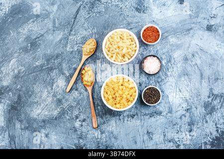 Un po' di pasta con spezie in ciotole bianche e cucchiai di legno su fondo in gesso grungy, piatto. Foto Stock