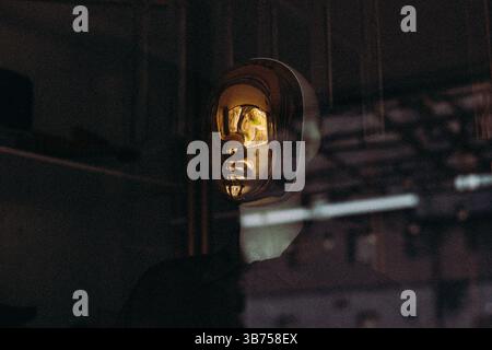 Una maschera dorata è collocata su uno sfondo scuro, riflettendo la luce e creando un'accattivante esposizione artistica. Il design elegante aggiunge un tocco di eleganza. Foto Stock