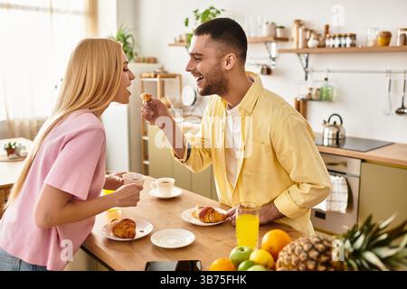 Gli amanti gioiosi condividono un delizioso pasto mattutino, nutrendosi a vicenda dei pasticcini in un ambiente vivace. Foto Stock