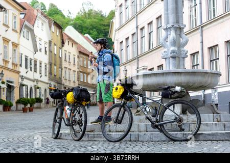Adolescente in un viaggio in bicicletta in Slovenia, ciclista che si gusta un gelato presso una fontana di Ercole nella parte storica vecchia di Lubiana, Sloven Foto Stock