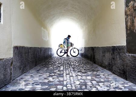 Adolescente in un viaggio in bicicletta per la Slovenia, ciclista in bicicletta in un tunel nella pittoresca parte vecchia di Lubiana, Slovenia Foto Stock