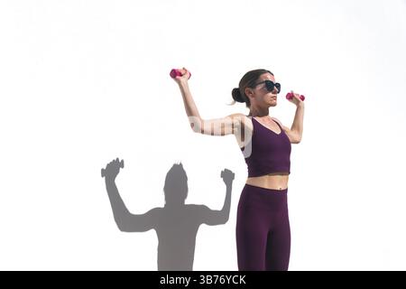 Donna atletica che fa esercizio con pesi a mano facendo esercizi al braccio all'aperto vicino a una parete bianca Foto Stock
