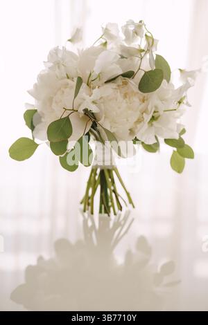 Bouquet nuziale di peonie bianche, piselli dolci e rami di eucalipto su un tavolo bianco lucido. Foto Stock