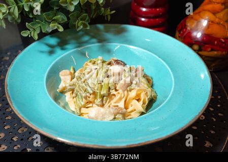 Deliziose tagliatelle cremose condite con asparagi verdi saltati e funghi serviti in un vivace piatto turchese. Foto Stock
