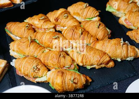 Mini panini con croissant preparati al momento, ripieni di lattuga, carne e formaggio, disposti su un vassoio di ardesia per un buffet servito. Foto Stock