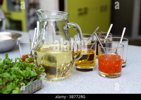 Una selezione di salse in tazze di vetro, compresi liquidi gialli, arancioni e limpidi, con erbe fresche in primo piano su un bancone della cucina. Foto Stock