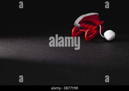 Berretto rosso di Babbo Natale sulla carrozza Red Wodden nella stanza buia. Babbo Natale dorme qui Foto Stock