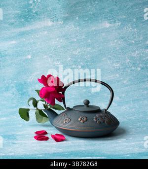 Teiera con fiori sul tavolo, bellissime rose rosse in teiera di ferro blu sullo sfondo blu. Messa a fuoco selettiva, copia spazio. Tè asiatico tradizionale c Foto Stock