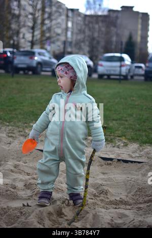 In primavera, la bambina gioca con una pala in una scatola di sabbia in un cortile posteriore. Foto Stock
