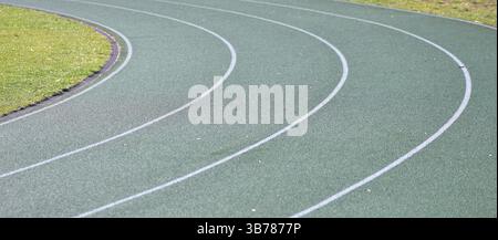 Curva verde della pista da corsa con linee bianche e erba verde sui lati. Piste sportive per stadi scolastici. Foto Stock