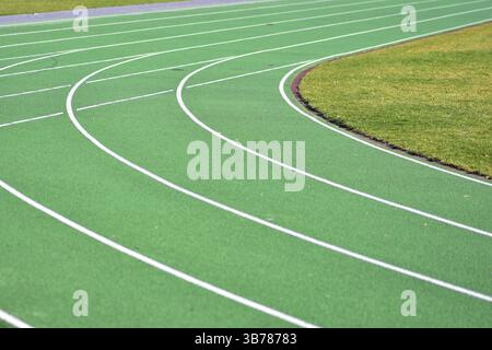 Curva verde della pista da corsa con linee bianche. Percorso pedonale sul lato sinistro e erba verde sul lato destro. Stadio scolastico, pista sportiva. Foto Stock