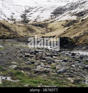 Poco profondo fiume di montagna, scorre dalle montagne innevate nella gola, su una cascata di cascate. Cima innevata della montagna e piedi in urlo Foto Stock