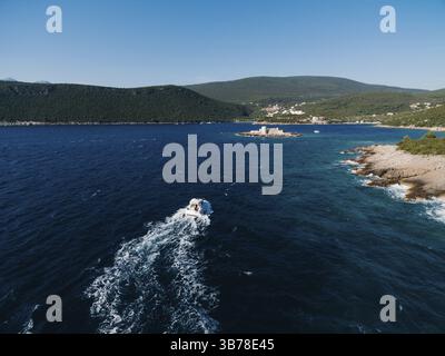 Il motoscafo bianco naviga lungo il mare verso la costa montuosa. Vista posteriore. Foto Stock