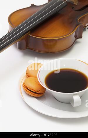 Pausa musicale - Vecchio violino, tazza di caffè e tradizionali macaron francesi colorati sul tavolo bianco Foto Stock