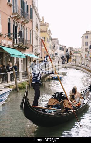 Venezia, Italia - 4 ottobre 2019: Matrimonio in Italia a Venezia. Un gondoliere rotola una sposa e uno sposo in una classica gondola di legno lungo una stretta cana veneziana Foto Stock