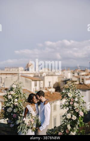 Coppia di nozze interrazziale. Matrimonio a Firenze, Italia. Una cerimonia nuziale sul tetto dell'edificio, con vista sulla città Foto Stock