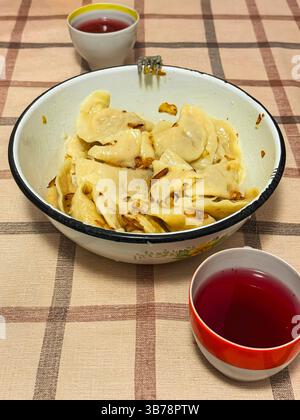 Gnocchi tradizionali con cipolle fritte serviti in una ciotola vintage con bevanda alla frutta, succo di frutta su un tavolo a scacchi. Cucina casalinga, comfort vintage Foto Stock